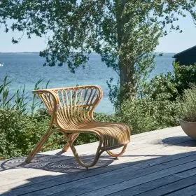 Sika-Design Fox Gartensessel in Natur auf Holzterrasse mit Meerblick, ohne Polster, stimmungsvolle Sommeratmosphäre.