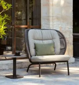 Vincent Sheppard Kodo Cocoon Outdoor Loungesessel in Grau, 100 cm, auf einer Terrasse mit Steinwand und Pflanzen im Hintergrund.