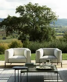 Zwei B&B Italia Borea Loungesofas stehen im Freien vor einer malerischen Landschaft mit einem Baum im Hintergrund und einem Tisch im Vordergrund.