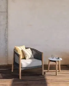Vincent Sheppard Lento Loungesessel in Grau mit Holzbeinen, auf einer Terrasse vor einer cremefarbenen Wand, neben einem kleinen Beistelltisch.