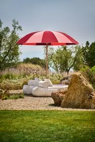 Pagodenschirm in Rosa-Bordeaux mit Holzstange, aufgestellt auf Betonboden neben einer Lounge mit cremefarbenem Badehandtuch.