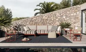 B&B Italia Ribes Outdoor Lounge auf einer Terrasse mit Steinmauer im Hintergrund und Palmen im Freien mit einem Pool im Vordergrund