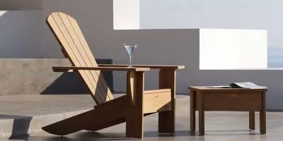 Royal Botania New England Gartenmöbel in Holzoptik, bestehend aus einem Sessel und einem Tisch, auf einer Terrasse mit Meerblick.
