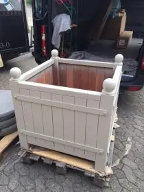 Orangerie Pflanzkübel aus lackiertem Akazienholz steht auf einer Palette vor einem Lieferwagen im Freien