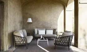 B&B Italia Erica Loungegruppe bestehend aus zwei Sesseln einem Sofa und einem Tisch in einem überdachten Außenbereich mit rustikaler Wand.