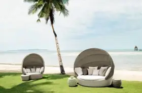 Dedon Orbit XXL Sofainsel auf einer grünen Wiese am Strand mit Palmen und Meer im Hintergrund