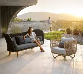 Cane-line Nest Loungegruppe in Schwarz und Grau auf einer Terrasse mit Bergblick bei Sonnenuntergang, entspannte Atmosphäre.