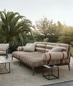 B&B Italia Ribes Outdoor Lounge auf einer Terrasse mit Palmen im Hintergrund und einem Beistelltisch auf einem Teppich.