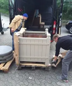 Zwei Männer entladen einen lackierten Orangerie Pflanzkübel aus Akazienholz aus einem Lieferwagen und entfernen die Verpackung.