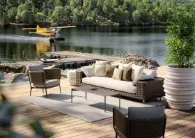DEDON BELLMONDE Gartenmöbel auf einer Terrasse am See mit einem Wasserflugzeug im Hintergrund und umgeben von Pflanzen und Bäumen