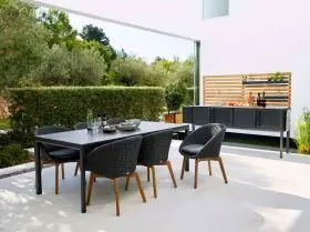 Cane-line Drop Küchenmodul Essgruppe in Schwarz auf einer Terrasse mit modernem Hintergrund und grüner Hecke.